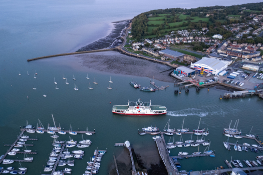 Aerial view of a Red Funnel ferry departing the harbor past a marina filled with sailboats and industrial buildings along the coastline in Cowes England United Kingdom.