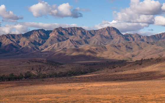 Aerial view of the rugged peaks and ancient geological formations of the Heysen mountain range under a blue sky with scattered clouds in Flinders Ranges South Australia Australia. Aerial view of the rugged peaks and ancient geological formations of the Heysen mountain range under a blue sky with scattered clouds in Flinders Ranges South Australia Australia.