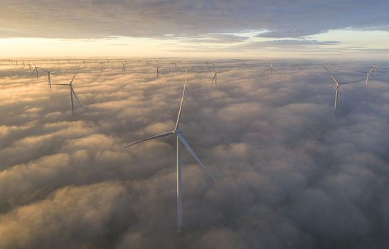 Aerial view of wind turbines rising above a thick layer of clouds during a golden sunrise with soft light illuminating the mist in Netherlands. Aerial view of wind turbines rising above a thick layer of clouds during a golden sunrise with soft light illuminating the mist in Netherlands.