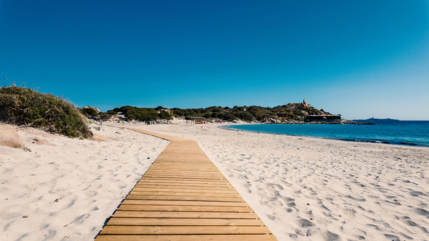 View of a wooden boardwalk leading across the white sand of Punta Molentis Beach towards the turquoise sea under a clear blue sky Villasimius Sardinia Italy. View of a wooden boardwalk leading across the white sand of Punta Molentis Beach towards the turquoise sea under a clear blue sky Villasimius Sardinia Italy.