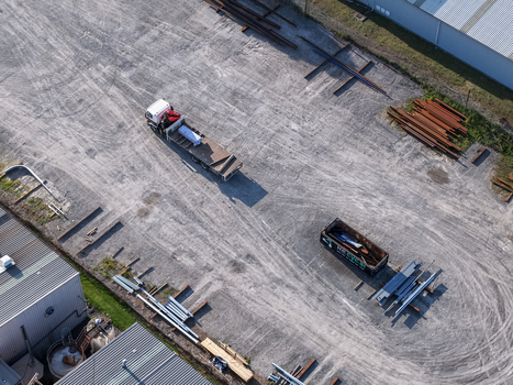Melbourne VIC Australia 22 September 2026 Aerial view of a flatbed truck in an industrial yard in Kilsyth with metal beams a dumpster and factory buildings. Melbourne VIC Australia 22 September 2026 Aerial view of a flatbed truck in an industrial yard in Kilsyth with metal beams a dumpster and factory buildings.