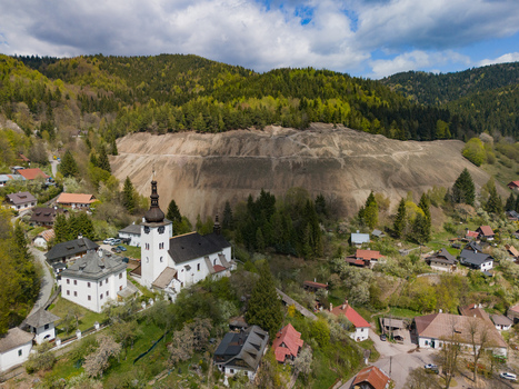 Aerial view of the historic village with its white church tower and traditional houses against a backdrop of mining heaps and green hills in Spania Dolina Banska Bystrica Region Slovakia.