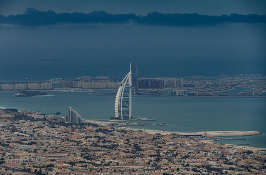 View of the Burj Al Arab hotel standing on the coastline with the Palm Jumeirah and city skyline under a dramatic cloudy sky in Dubai Dubai United Arab Emirates. View of the Burj Al Arab hotel standing on the coastline with the Palm Jumeirah and city skyline under a dramatic cloudy sky in Dubai Dubai United Arab Emirates.