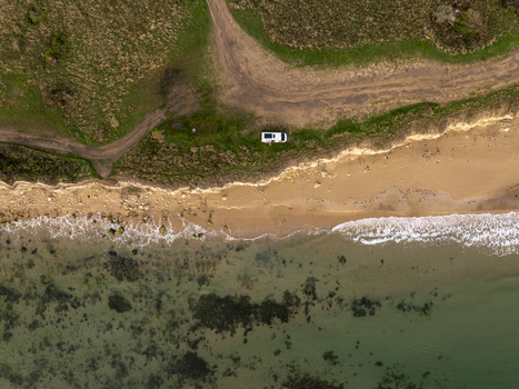 Aerial view of a camper van parked on the grassy cliff edge above a sandy beach with gentle waves and clear water in Nessebar Burgas Bulgaria. Aerial view of a camper van parked on the grassy cliff edge above a sandy beach with gentle waves and clear water in Nessebar Burgas Bulgaria.