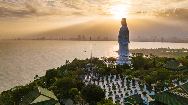 Aerial view of the giant Lady Buddha statue at Linh Ung Pagoda surrounded by a bonsai garden and temple architecture overlooking the ocean and city skyline at sunset in Da Nang Vietnam. Aerial view of the giant Lady Buddha statue at Linh Ung Pagoda surrounded by a bonsai garden and temple architecture overlooking the ocean and city skyline at sunset in Da Nang Vietnam.