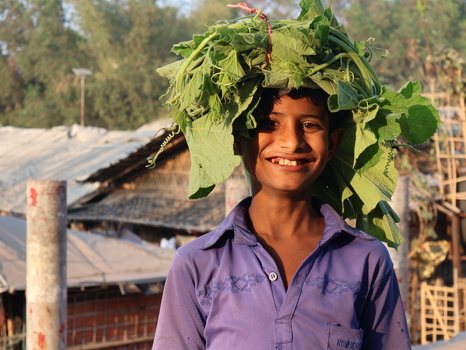 Cox s Bazar Chittagong Division Bangladesh 19 July 2026 View of a young boy smiling with a bundle of green leafy vegetables on his head in a refugee camp setting. Cox s Bazar Chittagong Division Bangladesh 19 July 2026 View of a young boy smiling with a bundle of green leafy vegetables on his head in a refugee camp setting.