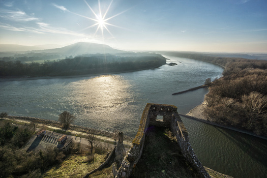 View of the historic stone walls of Devin Castle overlooking the wide river and distant hills under a bright sun star in Bratislava IV Bratislava Region Slovakia. View of the historic stone walls of Devin Castle overlooking the wide river and distant hills under a bright sun star in Bratislava IV Bratislava Region Slovakia.