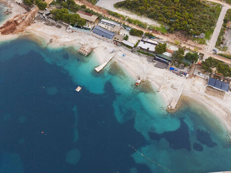 Aerial view of the turquoise waters and sandy coastline of Ksamil featuring beachside structures and lush greenery in Ksamil Vlore County Albania. Aerial view of the turquoise waters and sandy coastline of Ksamil featuring beachside structures and lush greenery in Ksamil Vlore County Albania.