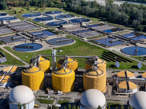 Aerial view of the Impianto depurazione water treatment plant featuring circular tanks yellow silos and white domes near the river in Castiglione Torinese Piedmont Italy.
