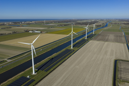 Aerial view of modern wind turbines and solar panels along a straight canal through polder agricultural fields with a road and vehicle under a clear blue sky in Netherlands. Aerial view of modern wind turbines and solar panels along a straight canal through polder agricultural fields with a road and vehicle under a clear blue sky in Netherlands.