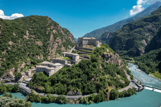 Aerial view of the historic Fort Bard on a rocky hill surrounded by lush green mountains and the Dora Baltea river Bard Aosta Valley Italy.