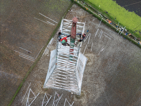 Trishal Upazila Bangladesh 13 May 2026 Aerial view of workers constructing a metal telecommunications tower over agricultural fields and green landscape. Trishal Upazila Bangladesh 13 May 2026 Aerial view of workers constructing a metal telecommunications tower over agricultural fields and green landscape.