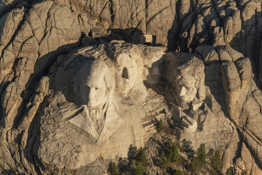 Aerial view of Mount Rushmore National Memorial featuring granite sculptures of US presidents carved into the mountain with pine trees in Keystone South Dakota United States. Aerial view of Mount Rushmore National Memorial featuring granite sculptures of US presidents carved into the mountain with pine trees in Keystone South Dakota United States.