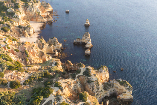 Aerial view of dramatic limestone cliffs and rock formations of Ponta da Piedade along the coastline with turquoise waters and winding footpaths in Lagos Faro District Portugal.