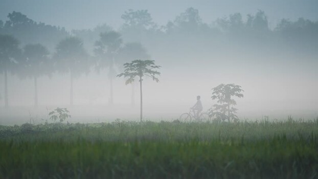 View of a person cycling through thick morning fog Bangladesh. View of a person cycling through thick morning fog Bangladesh.