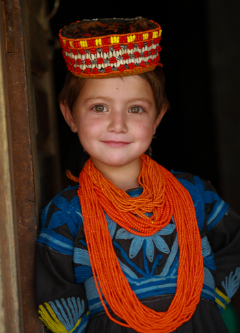 Chitral Khyber Pakhtunkhwa Pakistan 11 September 2006 View of a young Kalash girl wearing a traditional embroidered headdress and vibrant orange bead necklaces in Rumbur valley.
