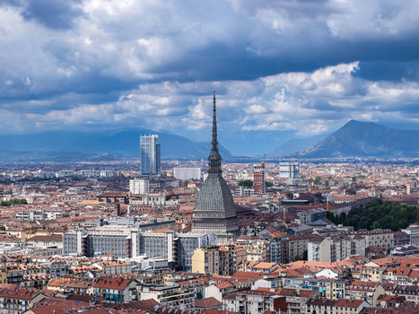 Aerial view of the Mole Antonelliana spire rising above the historic rooftops of the city with the Alps mountains under a cloudy sky in Turin Piedmont Italy. Aerial view of the Mole Antonelliana spire rising above the historic rooftops of the city with the Alps mountains under a cloudy sky in Turin Piedmont Italy.