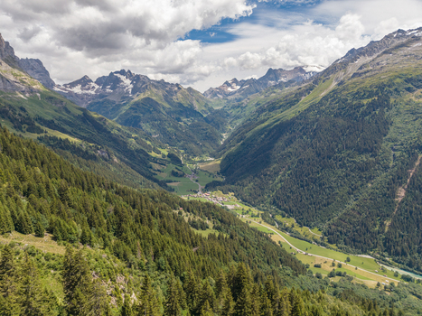 Aerial view of the Gadmen valley in the Swiss Alps featuring lush green meadows dense pine forests and rugged mountain peaks under a cloudy summer sky in Gadmen Switzerland.
