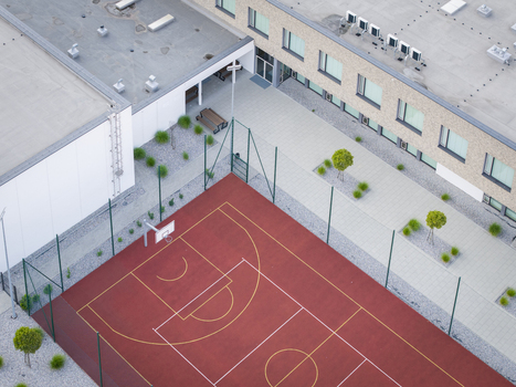 Aerial view of a red sports court with white markings situated next to a modern building with a paved courtyard and small trees in Wieliczka Lesser Poland Voivode Poland.