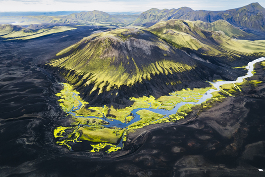 Aerial view of a moss covered volcanic cone surrounded by black sand plains and a winding river near the F232 road in Skaftarhreppur Iceland.