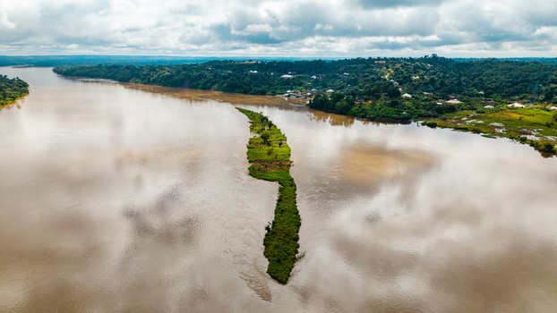 Aerial view of the Cross River flowing past a long narrow green island surrounded by lush vegetation and cloudy skies in Itu Akwa Ibom Nigeria. Aerial view of the Cross River flowing past a long narrow green island surrounded by lush vegetation and cloudy skies in Itu Akwa Ibom Nigeria.
