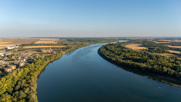 Aerial view of the Sava River winding through the landscape with lush forests agricultural fields and industrial facilities in Sremska Mitrovica Vojvodina Serbia.