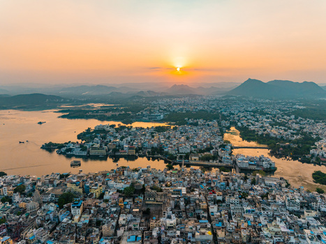 Aerial view of the historic city of Udaipur with its dense urban architecture and palaces situated along the shores of Lake Pichola during a golden sunset Udaipur Rajasthan India.
