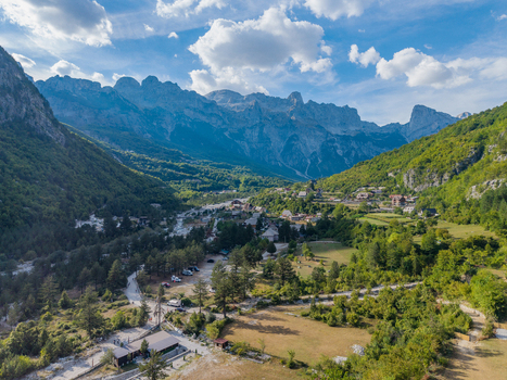 Aerial view of the village of Theth nestled in the Albanian Alps featuring traditional houses lush green meadows and dense forests under a bright blue sky Theth Shkoder County Albania. Aerial view of the village of Theth nestled in the Albanian Alps featuring traditional houses lush green meadows and dense forests under a bright blue sky Theth Shkoder County Albania.