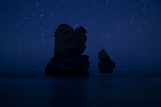 View of the silhouetted limestone stacks of the Twelve Apostles under a night sky with star trails in Twelve Apostles Marine National Park Australia. View of the silhouetted limestone stacks of the Twelve Apostles under a night sky with star trails in Twelve Apostles Marine National Park Australia.