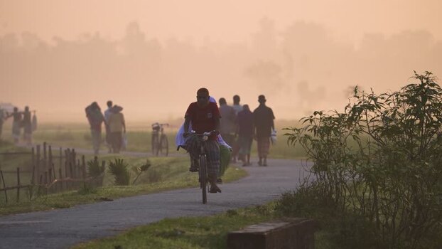 View of a man riding a bicycle on a misty road in Bogura Bangladesh.