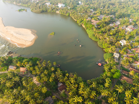 Aerial view of a calm lagoon meeting the ocean with a sandy beach and dense palm trees in Galle Southern Province Sri Lanka.