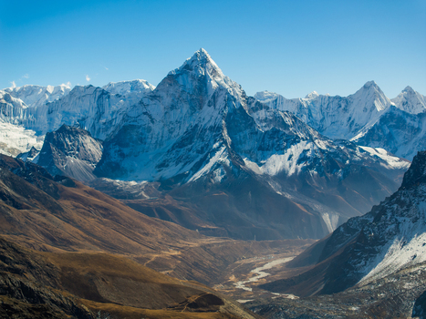 Aerial view of the majestic Ama Dablam mountain peak rising above the rugged Himalayan landscape with snow covered slopes and a deep valley in Nepal.