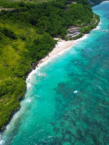 Aerial view of Pantai Nunggalan featuring turquoise waters white sand and lush green cliffs in Kecamatan Kuta Selatan Bali Indonesia.