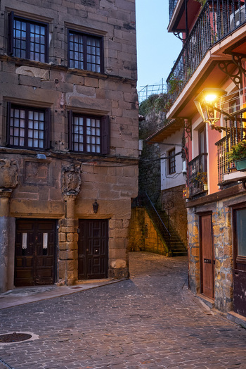 Pasai Donibane Spain 09 March 2026 View of the historic harbor street with narrow cobblestone paths traditional stone buildings and a glowing street lamp at dusk.
