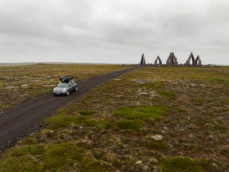 Aerial view of a car driving on a gravel road towards the Arctic Henge monument set in a vast mossy landscape under a cloudy sky in Raufarhofn Nordurthing Iceland.