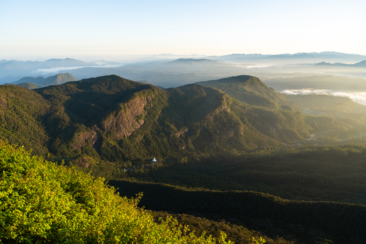 View of Adam s Peak and the surrounding lush mountain ranges with a white stupa in the valley and morning mist under a clear sky Ratnapura Sabaragamuwa Province Sri Lanka. View of Adam s Peak and the surrounding lush mountain ranges with a white stupa in the valley and morning mist under a clear sky Ratnapura Sabaragamuwa Province Sri Lanka.