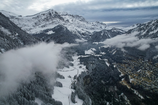 Aerial view of Les Rives and the snowy alpine valley with mist over pine forests and rugged peaks in Champery Valais Switzerland.