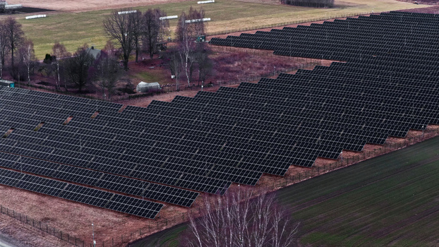 Aerial view of a large solar farm with rows of photovoltaic panels installed in a rural field surrounded by trees and agricultural land in Latvija. Aerial view of a large solar farm with rows of photovoltaic panels installed in a rural field surrounded by trees and agricultural land in Latvija.