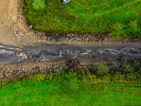Aerial view of a winding muddy path cutting through lush green meadows in the countryside of Latvia.