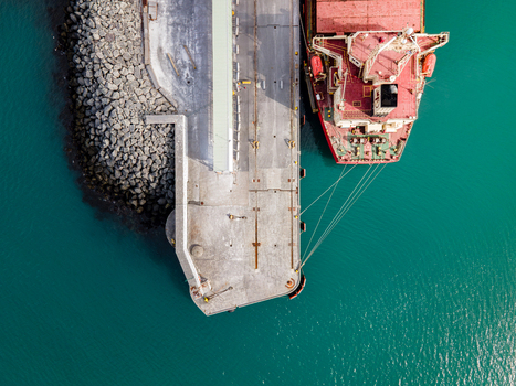 Aerial view of a large red cargo ship moored at the industrial port next to turquoise water and a stone breakwater in Hafnarfjordur Hafnarfjardarkaupstad Iceland. Aerial view of a large red cargo ship moored at the industrial port next to turquoise water and a stone breakwater in Hafnarfjordur Hafnarfjardarkaupstad Iceland.