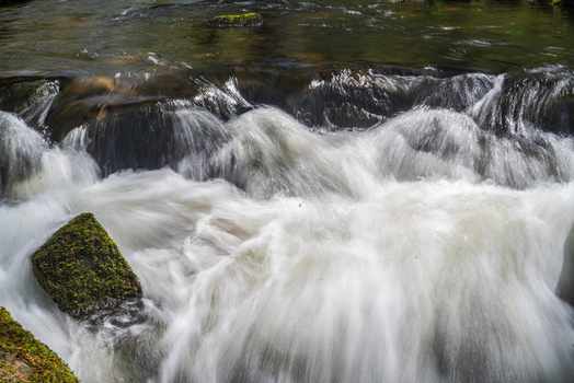 View of the rushing water and moss covered rocks at Golitha Falls National Nature Reserve in Liskeard England United Kingdom. View of the rushing water and moss covered rocks at Golitha Falls National Nature Reserve in Liskeard England United Kingdom.
