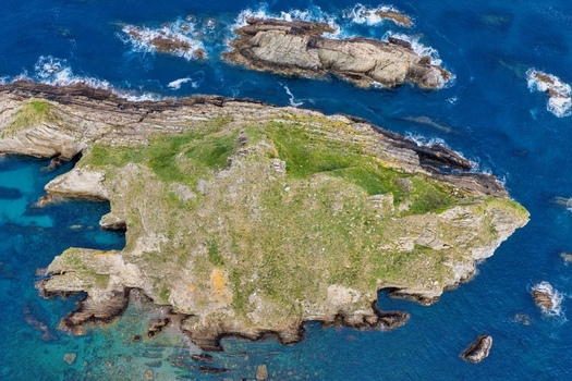 Aerial view of the rocky islet near Silence Beach Viewpoint with green vegetation and crashing waves in the blue sea of Cudillero Asturias Spain.