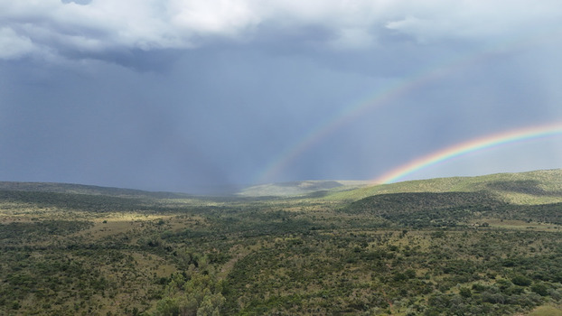Aerial view of a double rainbow stretching across rolling green hills and dense bushveld under a dramatic stormy sky in Waterberg District Municipality Limpopo South Africa. Aerial view of a double rainbow stretching across rolling green hills and dense bushveld under a dramatic stormy sky in Waterberg District Municipality Limpopo South Africa.