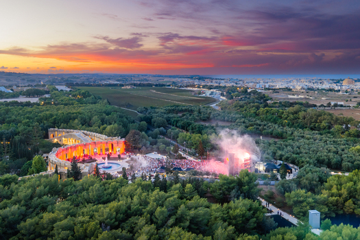 Aerial view of Park Nazzjonali Ta Qali during an outdoor concert at sunset featuring a fountain crowd stage lighting and lush greenery in Attard Northern Region Malta. Aerial view of Park Nazzjonali Ta Qali during an outdoor concert at sunset featuring a fountain crowd stage lighting and lush greenery in Attard Northern Region Malta.