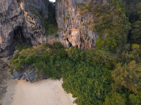 Aerial view of jagged limestone cliffs embrace a secluded sandy cove where emerald foliage meets the turquoise sea Railay Beach Thailand.