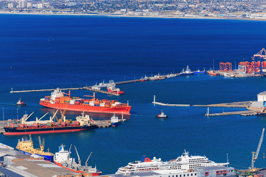 Aerial view of ships docked at the vibrant harbor where deep blue waters meet the industrial landscape framed by the distant city skyline Cape Town Western Cape South Africa.