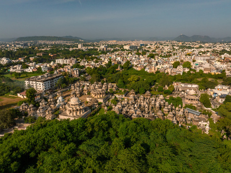 Aerial view of the historic Ahar Cenotaphs featuring numerous stone domes and monuments surrounded by lush green trees and the urban cityscape of Udaipur Rajasthan India.