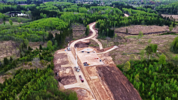 Aerial view of wind turbine foundation construction site with a crane and heavy machinery in a forested landscape in Latvia. Aerial view of wind turbine foundation construction site with a crane and heavy machinery in a forested landscape in Latvia.