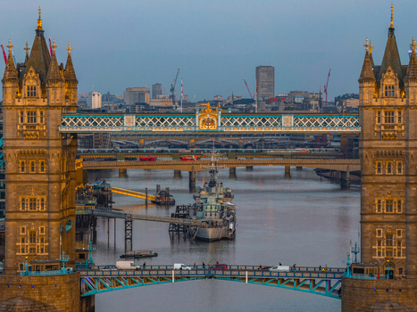 Aerial view of Tower Bridge spanning the River Thames with the historic HMS Belfast moored nearby and the urban skyline of London England United Kingdom. Aerial view of Tower Bridge spanning the River Thames with the historic HMS Belfast moored nearby and the urban skyline of London England United Kingdom.