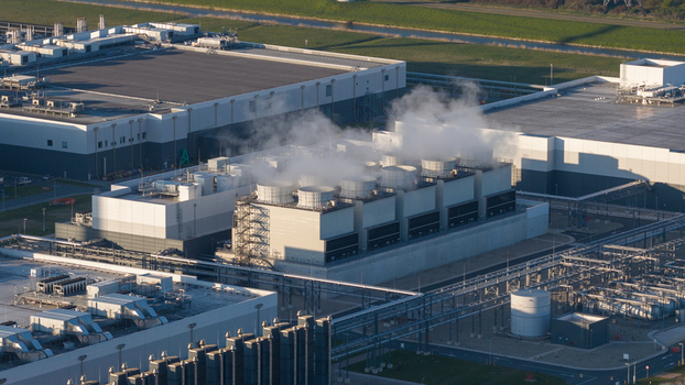 Aerial view of the cooling towers of a large industrial data center facility with steam rising against a backdrop of modern buildings and green fields in Eemshaven Groningen Netherlands. Aerial view of the cooling towers of a large industrial data center facility with steam rising against a backdrop of modern buildings and green fields in Eemshaven Groningen Netherlands.